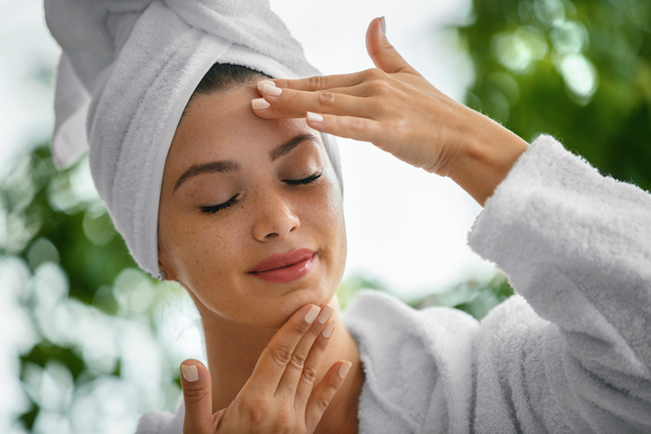 Young woman massaging face with her eyes closed. She's in the bathrobe and her hair is wrapped in the towel.